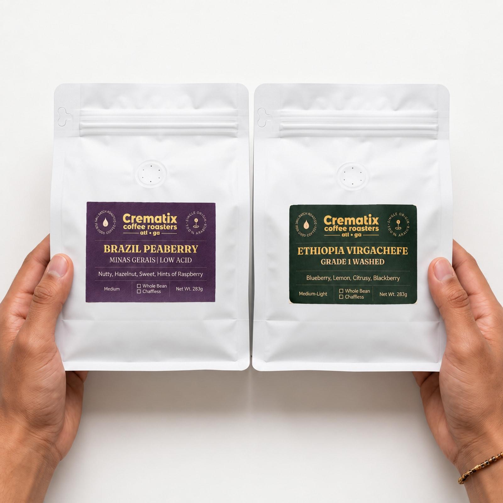Hands holding two white Crematix coffee bags: Brazil Peaberry on the left and Ethiopia Yirgachefe G1 Washed on the right.